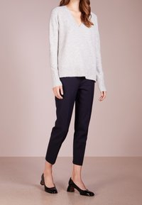 Suéter de cuello en V gris claro, con dobladillo y puños acanalados, combinado con pantalones oscuros de corte tapered en color marino y mocasines negros de charol con tacón cuadrado.