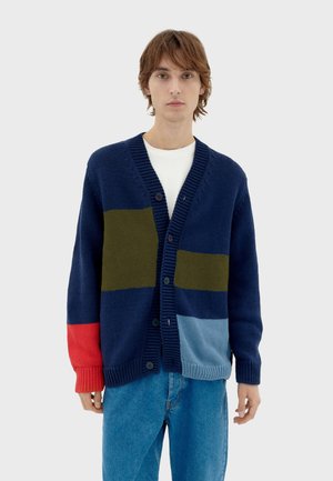 Cárdigan de punto en navy con paneles de rayas verticales en verde, rojo y azul claro, con escote en V y cierre de botones.