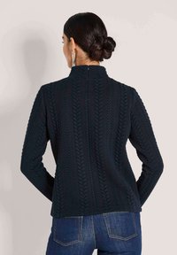 Dunkelblaues Strickpullover mit einem strukturierten Kabelmuster, taillierter Schnitt mit hohem Kragen und langen Ärmeln, kombiniert mit blauen Jeans.