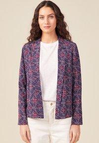Blazer a fantasia in blu navy con dettagli floreali multicolori. Tessuto leggero, chiusura a un bottone e vestibilità sartoriale. Abbinato a un top bianco.