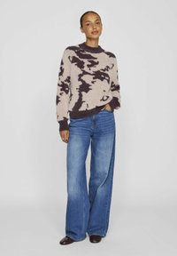 Pull en tricot doux, beige avec un motif abstrait violet foncé ; col rond ; associé à un jean en denim bleu à jambes larges ; tissu texturé.