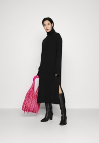 Schwarzes Rollkragenkleid mit seitlichem Schlitz, kombiniert mit kniehohen schwarzen Stiefeln und einer lebhaften pinkfarbenen geflochtenen Tasche. Glatte Textur, minimalistisches Design.