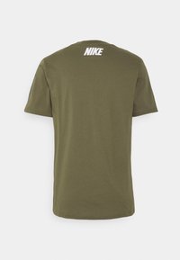 Olivově zelené tričko s krátkým rukávem vyrobené z bavlny. Na horní části zad se nachází bílé logo Nike. Hladká textura, volný střih.
