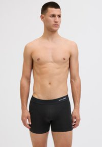 Schwarze Boxerbriefs aus weichem Material, mit einem glatten Bund mit "JACK & JONES"-Logo und einem taillierten Schnitt, der bis zur Mitte des Oberschenkels reicht.