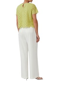 Jasnozielony top z dziurkami z falbaniastym dołem i dekoltem w kształcie dziurki z tyłu, zestawiony z białymi szerokimi spodniami i sandałami na obcasie.