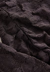 Tissu violet foncé avec un motif en dentelle complexe comprenant des dessins floraux et géométriques, présenté avec des plis doux et des détails de texture.