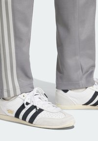 Grå träningsbyxor med vita ränder på sidorna, tillsammans med vita sneakers med marinblå ränder och texturerade detaljer.