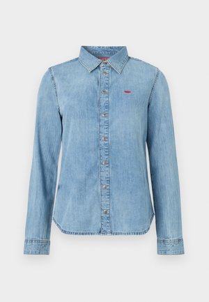 Light blue denim shirt with a pointed collar, front button closure, and a small red logo on the chest. Long sleeves with buttoned cuffs.