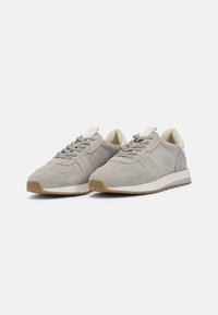 Grå semsket sneakers med teksturert overflate, rund tå, grå snørebånd og hvite detaljer på hælen og tungen. Gummisåle for godt grep.