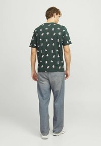 Grøn kortærmet t-shirt med et gentaget mønster af tegneserie-snefnug, parret med lyseblå baggy jeans og hvide sneakers.