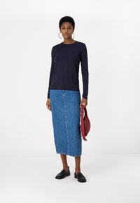 Μπλε μπλουζάκι με μακριά μανίκια συνδυασμένο με τζιν φούστα μέχρι το γόνατο, κρατώντας μια κόκκινη τσάντα. Μαύρα μοκασίνια ολοκληρώνουν το ντύσιμο. Απλή παλέτα χρωμάτων.