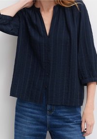 Camicia blu navy con colletto cinese, realizzata in un tessuto testurizzato, con sottili righe verticali e maniche a tre quarti.