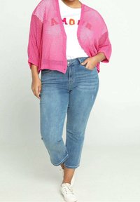 Rosa öppet stickad cardigan över en vit T-shirt med texten "AMOUR", i kombination med ljusblå beskurna jeans och vita sneakers.