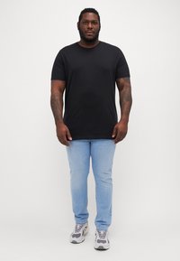 Čierne bavlnené tričko s krátkymi rukávmi, v kombinácii s svetlo modrými slim-fit džínsami a sivými teniskami. Jednoduchý dizajn, bez viditeľných vzorov alebo akcentov.
