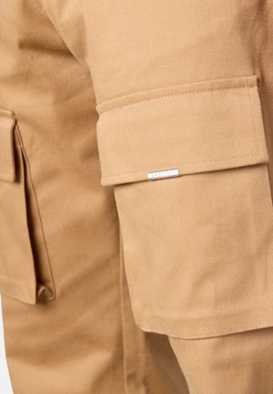 Khaki Cargo-Hosen aus strapazierfähigem Stoff, mit seitlichen Taschen und einem kleinen Metall-Logo. Glatte Textur mit sauberer Naht.