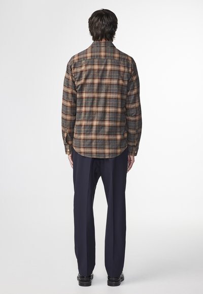 Plaid shirt in brown and blue tones, long sleeves, buttoned cuffs, and a curved hem. Worn with navy trousers and black shoes.