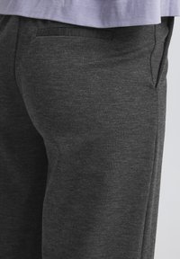 Tmavě šedé tepláky s jemnou texturou, jednou zadní kapsou a zúženým střihem. Látka má jemně melírovaný vzor.