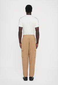 Pantalons cargo beiges avec taille élastique et poches latérales, associés à un T-shirt blanc à manches courtes avec des accents noirs aux épaules.