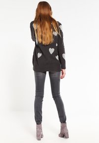 Tmavě šedý svetr se stříbrnými vzory srdce, doplněný šedými džíny a šedými kotníkovými botami. Svetr má uvolněný střih a ribbovaný spodní lem.