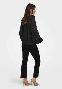 Blusa nera trasparente a pois con maniche ampie e svolazzanti, abbinata a jeans neri a vita alta e scarpe con tacco nudo.