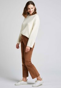 Un pull ample en ivoire, en tissu texturé, associé à un pantalon en velours côtelé marron et des baskets blanches, créant ainsi une tenue décontractée.