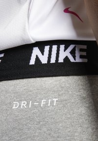 Nike Dri-FIT materials; white fabric with a pink logo, black waistband with white "NIKE," and grey textured fabric below.