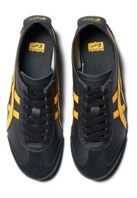 Svarta och gula sportskor med en texturerad läder- och mockaovandel, med snörningsdesign och gummisula, visade uppifrån.