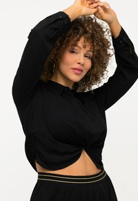 Sort cropped bluse med en snoet frontdetalje, lange ærmer og knapmanchetter. Glat stof, båret med et bælte med guldstriber.