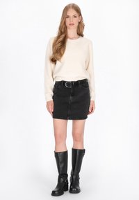 Crème gebreide trui, zwarte denimrok met riem en zakken, zwart leren laarzen tot de knie met gespen. Eenvoudig en functioneel ontwerp.