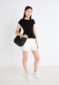 Black short-sleeve top with ruffle detail, white eyelet shorts, and a black bag with a soft, rounded shape. White sneakers, simple design.