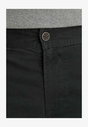 Pantalon vert foncé avec un bouton portant l'inscription « PME Legend Jeans » attaché sous la ceinture côtelée grise d'un pull.