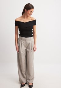 Top nero a spalla scoperta a coste abbinato a pantaloni ampi a pieghe grigio chiaro e ballerine nere a punta. Texture lisce e vestibilità aderente.