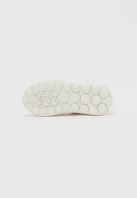 Fehér gumitalp lekerekített kialakítással. Kör alakú kiemelkedő mintázatokkal és szellőzőlyukakkal rendelkezik, amelyek tapadást és rugalmasságot biztosítanak.