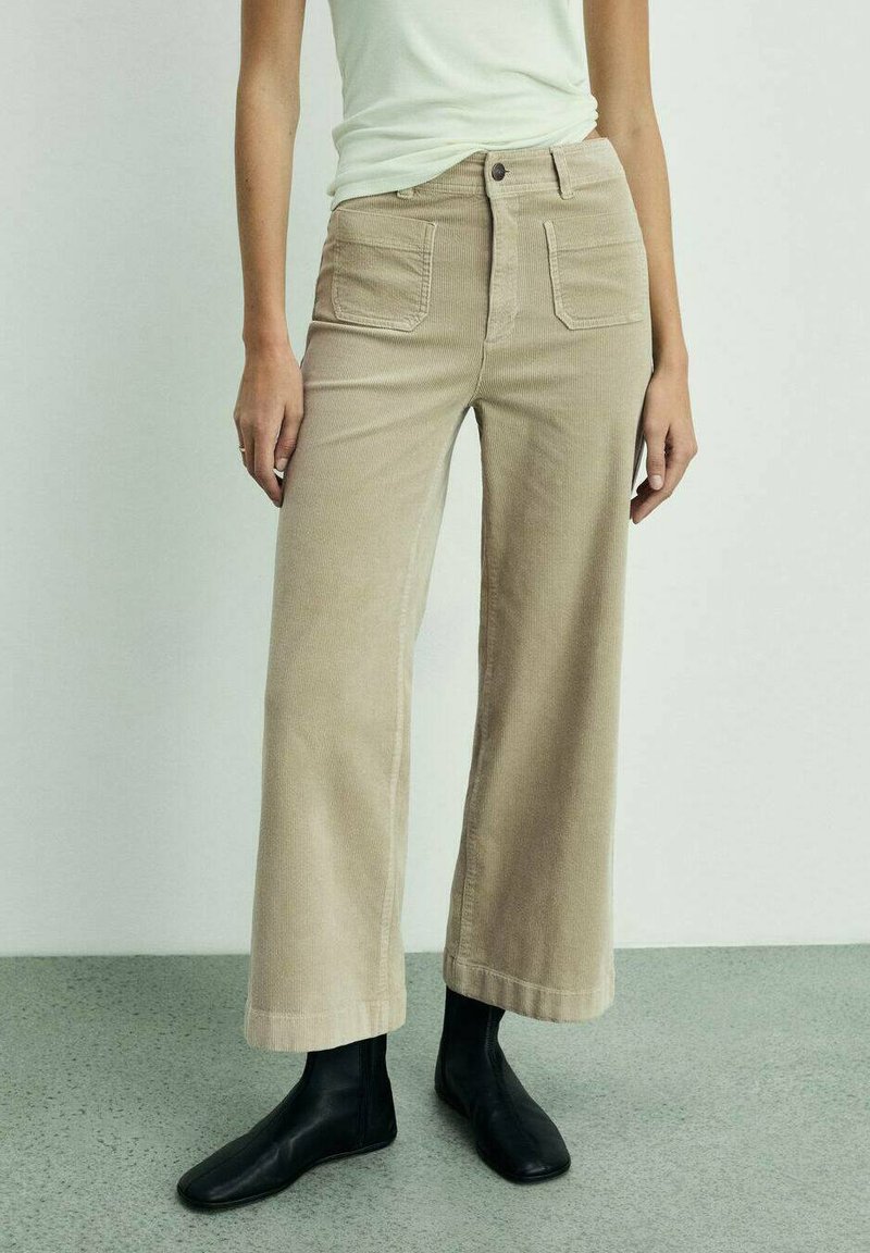 Beige corduroy wide-leg trousers with front pockets, high waist, and a subtle texture. Paired with black ankle boots.