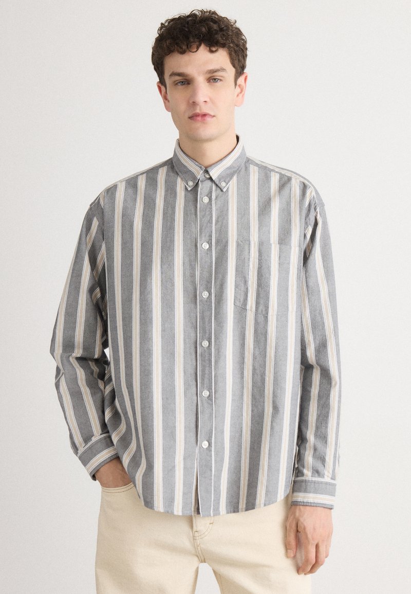 Camicia a righe grigie e bianche con colletto, maniche lunghe e taschino sul petto; realizzata in tessuto morbido, vestibilità casual.