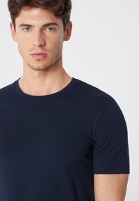 Námořnickomodré tričko s krátkým rukávem a kulatým výstřihem. Měkká, hladká textura, přiléhavý střih a bezešvý design ramen.