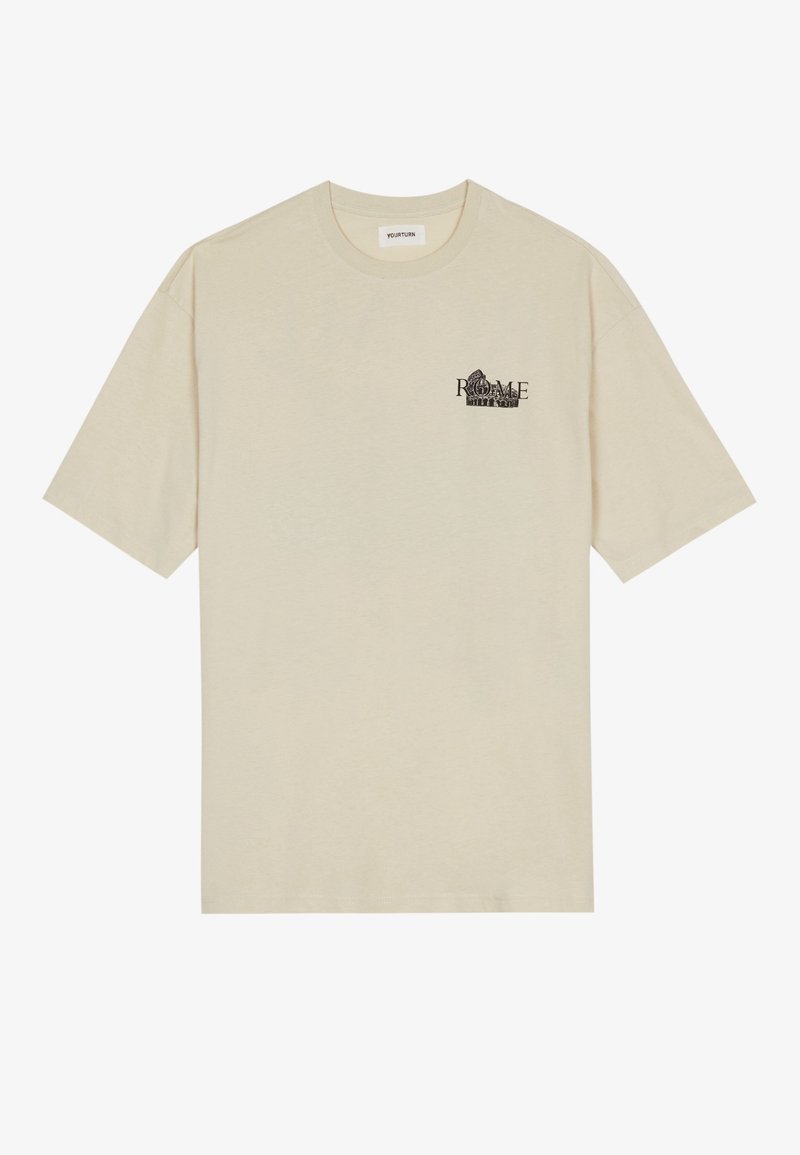 Camiseta de manga corta beige con cuello redondo, pequeño texto negro "ROMA" y un gráfico de arquitectura romana en el lado izquierdo del pecho.