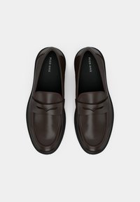 Mørkebrun skinnloafers med rund tå, flat såle og dekorativ frontrem. Innvendig har de merkeinformasjon. Glatt tekstur.