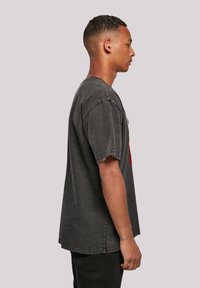 Dunkelgraues, übergroßes T-Shirt mit kurzen Ärmeln und rohem Saum. Strukturierter Stoff mit ausgewaschenem Finish und einem abstrakten grafischen Design auf der Vorderseite.