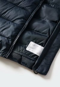Primer plano de una chaqueta acolchada negra con un zipper parcialmente abierto y una etiqueta interior para escribir el nombre y los datos de contacto.