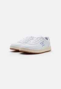 White leather sneakers with round toe, textured upper, and contrasting tan rubber sole. Features handwritten text on the side.
