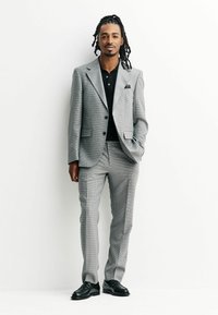 Gray checkered suit with a slim fit, featuring a black polo shirt underneath. Black dress shoes complete the look. Smooth texture, tailored design.
