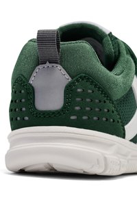 Grön sportskor med texturerad tyg, mockaskinndetaljer, grå detaljer, perforerade områden och en vit sula. Har en dragflik vid hälen.