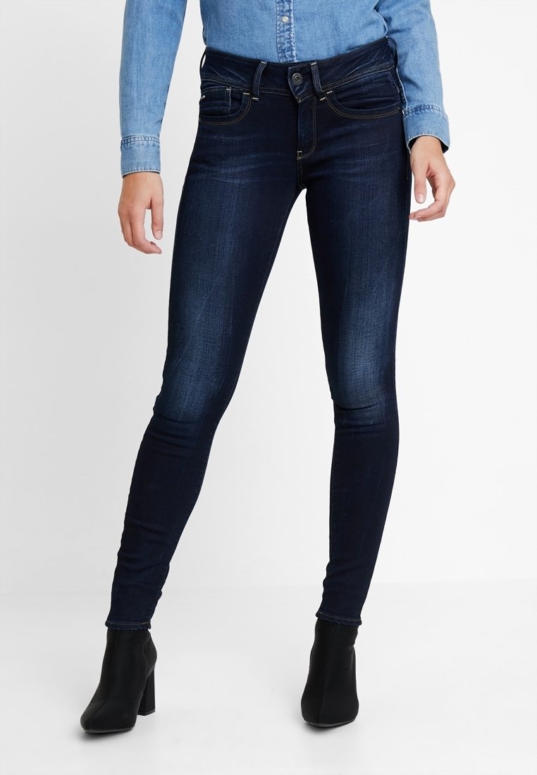 Jeans ajustados de color azul oscuro, confeccionados en denim con una textura suave, que presentan costuras decorativas, bolsillos delanteros y un cierre de botón.