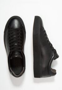 Paired de baskets en cuir noir avec semelles en caoutchouc épaisses, lacets et col rembourré vues de dessus et de côté sur fond blanc.