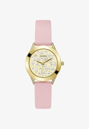 Zlaté hodinky Guess s ružovým silikónovým remienkom, zdobený ciferník s perlami a kryštálmi a tri zlaté ručičky ukazujúce čas.