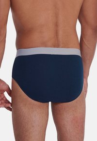 Slips blu navy con una cintura grigia chiara. Tessuto liscio ed elastico che si adatta al corpo. Presenta cuciture minime e un taglio classico.