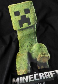 T-shirt med grafik som visar en grön blockig karaktär med ett pixelerat ansikte mot en svart bakgrund, med "Minecraft"-text under.
