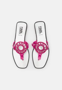 Vaaleanpunaiset litteät sandaalit, joissa on pyöreä leikkauksella varustettu muotoilu, erityisesti synteettisestä materiaalista valmistettu hihna ja kontrastivärinen valkoinen sisäpohja. Musta ulkopohja korostaa suunnittelua.