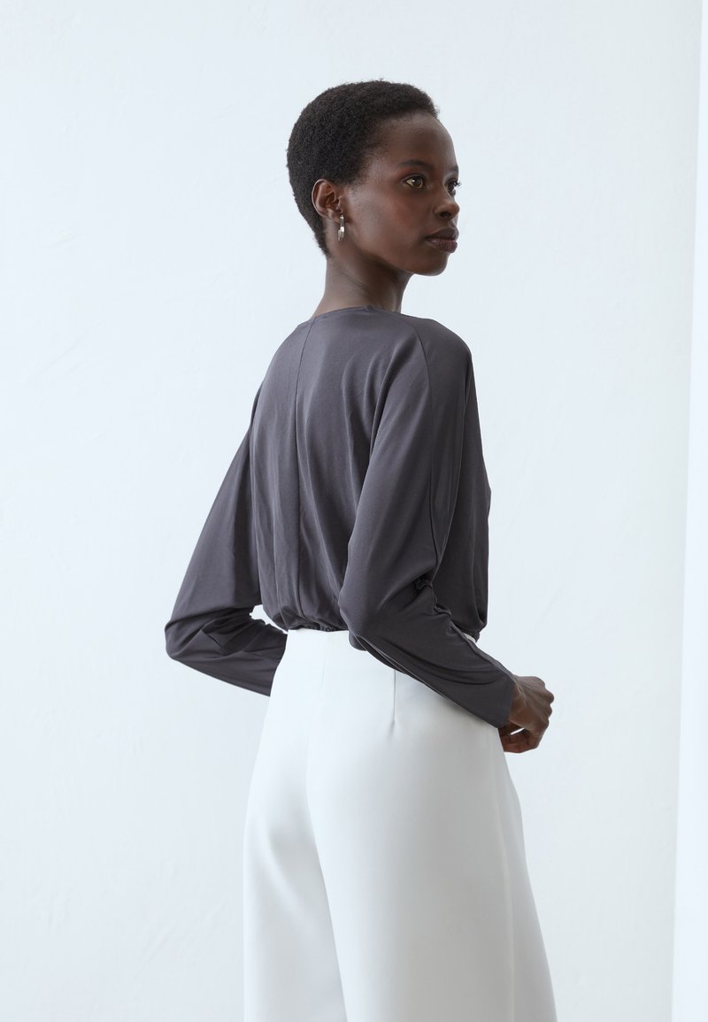 Szary długi rękaw top o luźnym kroju, zestawiony z białymi spodniami z wysokim stanem. Gładki, lekki materiał o subtelnym połysku.